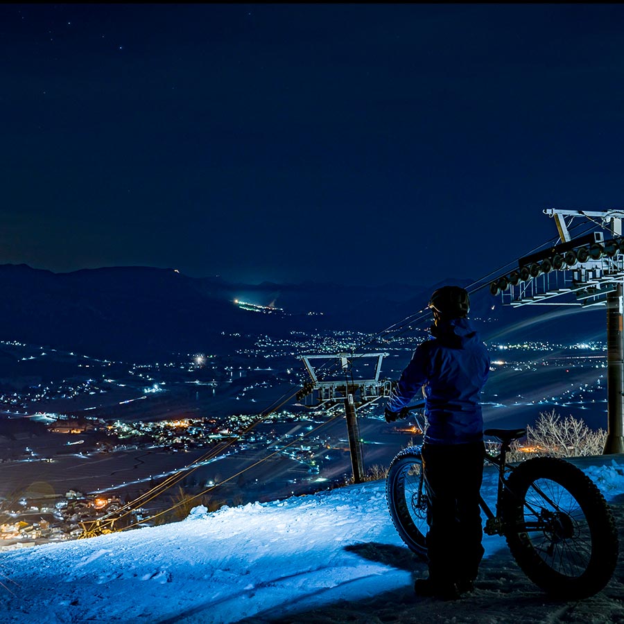 男性が雪ちゃりナイターで景色と写真をとっている