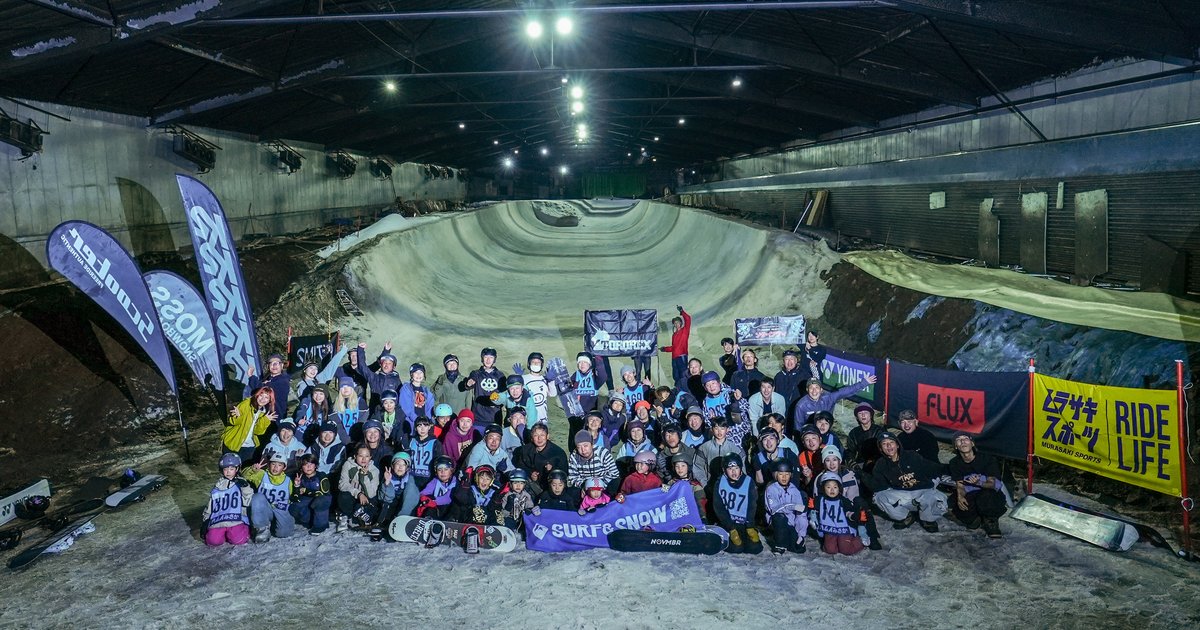 カムイみさかの屋内ハーフパイプ前で協賛ブランドのフラッグを背に並ぶ参加者の集合写真